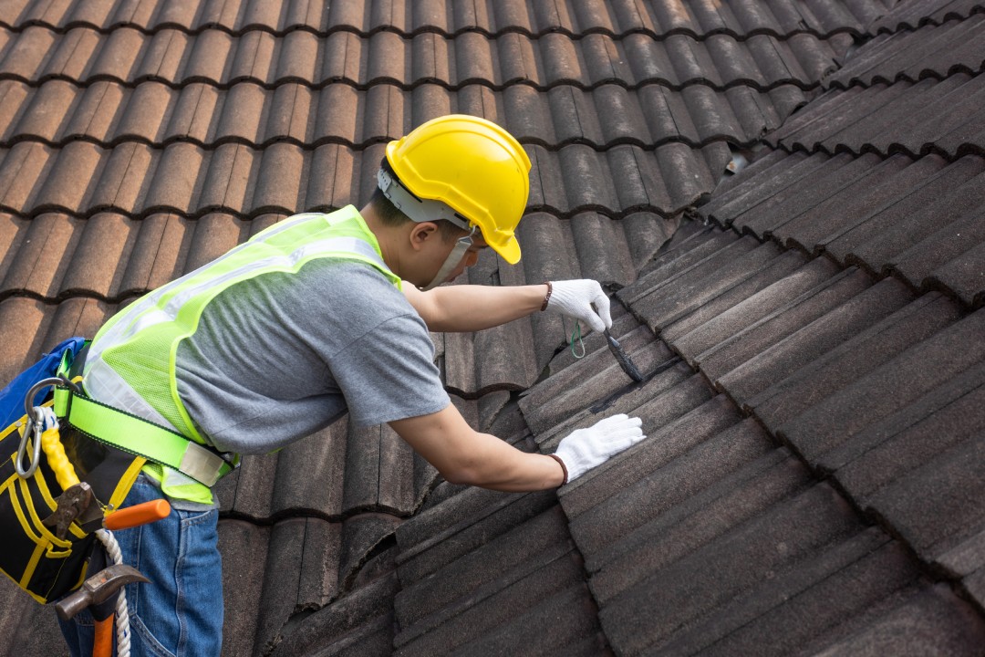 Worker man using waterproof roof coating repair to fix crack of the old tile roof.