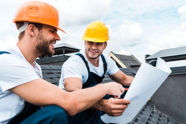 selective focus of happy builder looking at coworker and holding blueprint