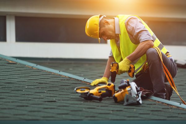 Roofer working in protective work wear gloves, using or building construction electric tool on top of the new roof under construction residential building