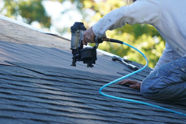 handyman using nail gun to install shingle to repair roof