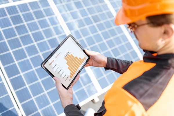 Trabajador examinando la generación de una planta de energía solar, sosteniendo una tableta digital con un gráfico de la producción de electricidad. Concepto de supervisión en línea de la central eléctrica