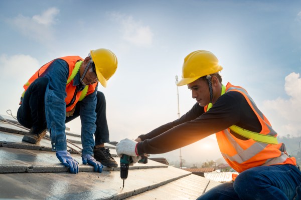Trabajador de la construcción con cinturón de arnés de seguridad durante el trabajo en la estructura del techo del edificio en la obra, Roofer utilizando aire o pistola de clavos neumática y la instalación de tejas de hormigón en la azotea superior.
