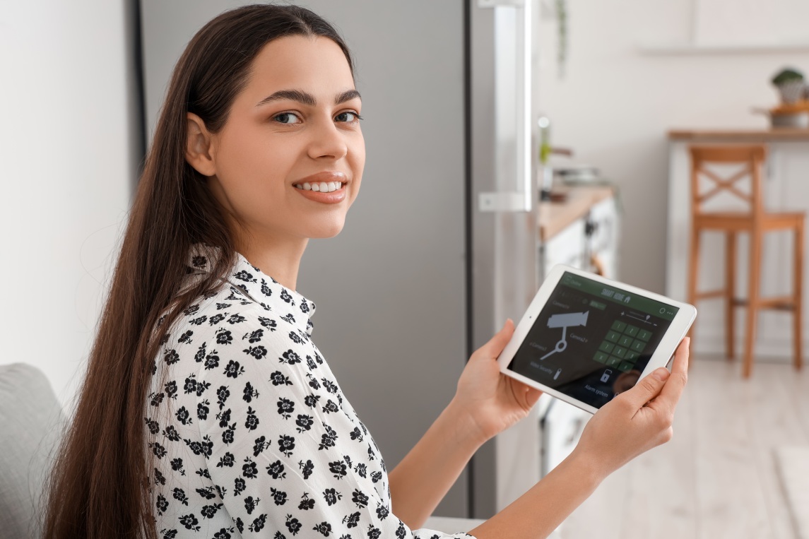 Young woman with smart home security system control panel in kitchen, closeup