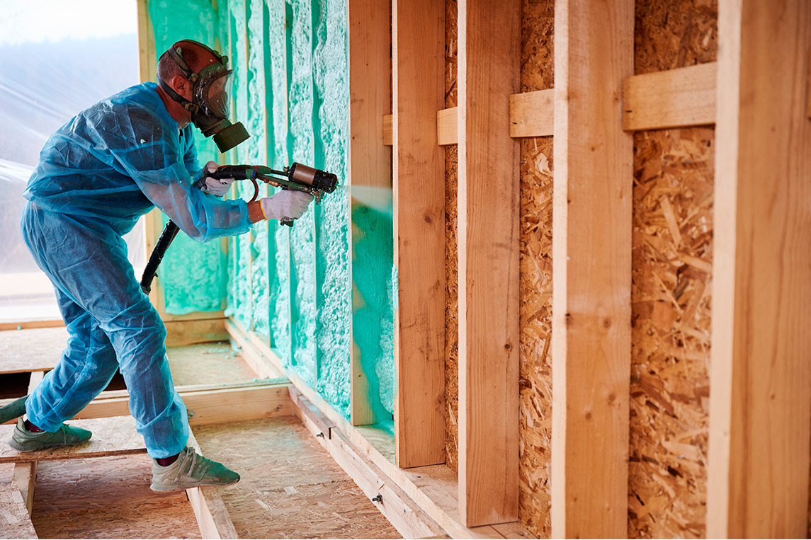 A man in a blue suit sprays insulation, promoting energy efficiency in a guide about spray foam savings in RGV.